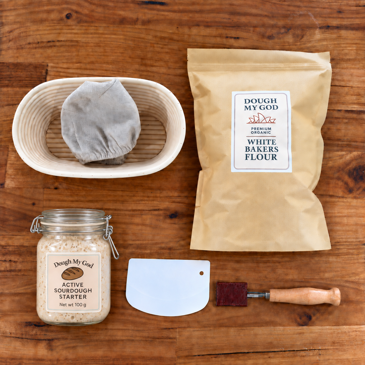 Essential sourdough starter kit with bubbling live starter in a closed-lid jar, organic bakers flour, oval banneton, dough lame and scraper