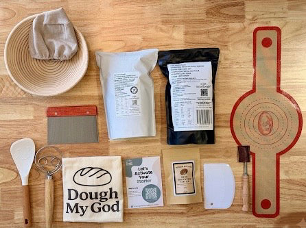 Gluten free sourdough baking kit and gluten free flour. Baking supplies including a bowl, scraper, and various packages on a wooden surface.