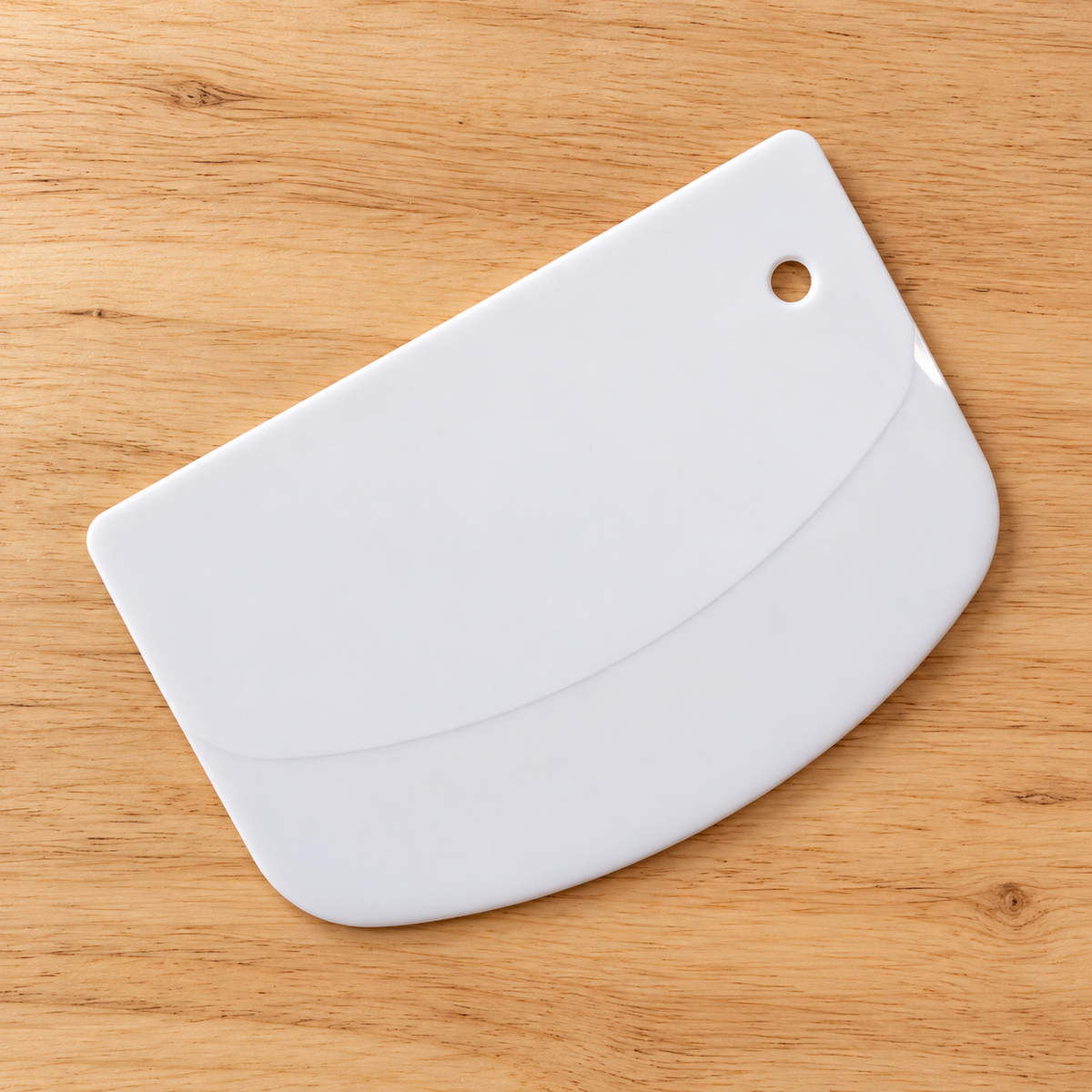 White flexible dough scraper on a natural timber surface