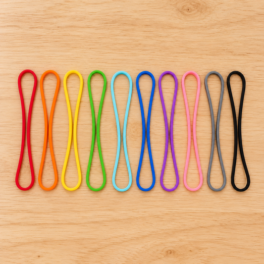 Ten coloured silicone sourdough starter feed bands on a light timber surface